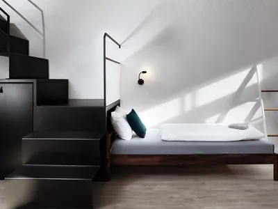 Minimalist bedroom with a wooden full-length bed, white bedding, and a black staircase leading to a cabinet.