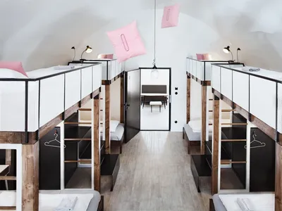 A minimalist bedroom with wooden bunk beds, white bedding, and hanging pink pillows.