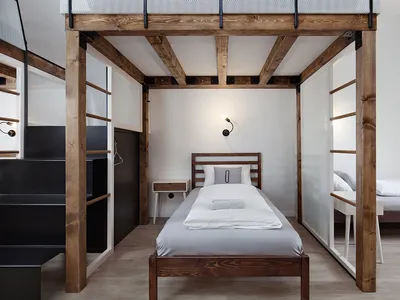 A minimalist bedroom with a single bed on a raised wooden frame, surrounded by transparent glass walls and metal railings.