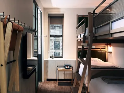 A minimalist bedroom features modern bunk beds made of wood with a ladder, a small table with a retro phone, and a window wit