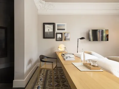A minimalist bedroom with a wooden desk, black chair, framed pictures, and a bed.