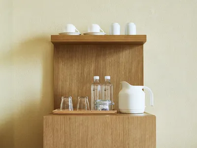 Minimalist office kitchen break room wooden shelf with white mugs, water bottles, and a white kettle.