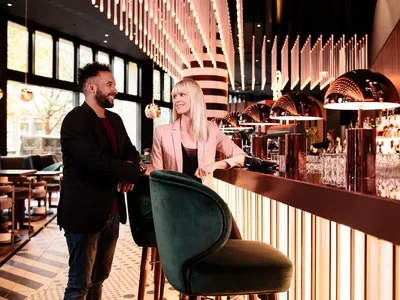 A modern bar with metallic black elements, featuring a smiling man and a woman sitting at the counter.