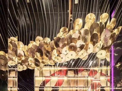 A modern hotel lobby adorned with metallic plates hanging from the ceiling and a curved glass wall.