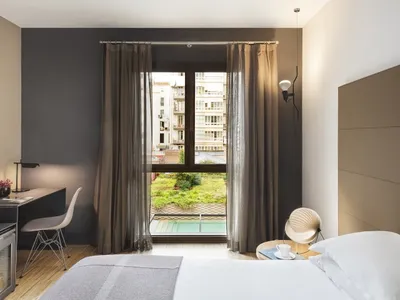 A modern hotel room with textured cotton blend materials, featuring a king-sized bed, desk, and large window overlooking a ga
