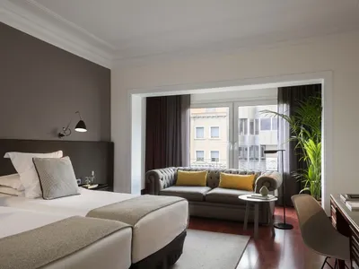 Modern, minimalist hotel suite with grey decor, featuring a comfortable seating area, a large bed with plush bedding, and a s