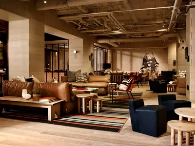 Modern lounge area with leather sofas, wooden tables, and concrete flooring in a hotel setting