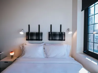 A modern minimalist bedroom featuring a black and white plaid upholstered headboard, white bedding, and a large window provid