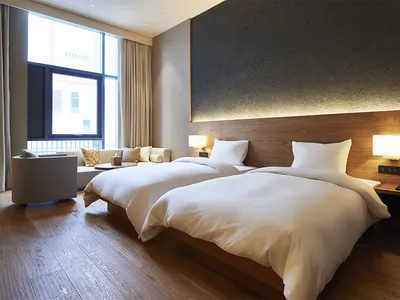 A modern, minimalist hotel room featuring wooden furnishings and fabric bedding.
