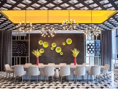 Modern restaurant dining room featuring concrete walls, glass ceiling accents, and a long dining table surrounded by white ch