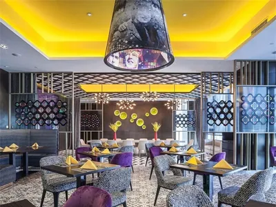 A modern restaurant interior with purple chairs, yellow napkins, and a geometric pattern on the ceiling and walls.