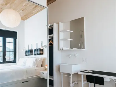 A minimalist bedroom with a white bed, wooden floor, and wooden ceiling.