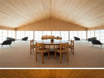 Modern restaurant interior with wooden tables and chairs, large windows, and a high wooden ceiling.