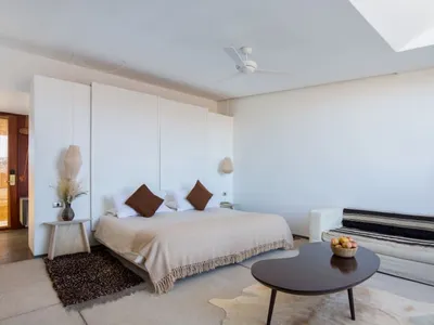 A modern bedroom with neutral-colored walls, a beige bedspread, and a white couch.