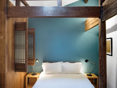A minimalist bedroom with blue walls and wooden furniture, featuring a comfortable bed with white bedding and two bedside tab