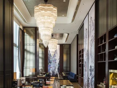 Modern hotel lobby with marble flooring, chandeliers, and seating arrangements.