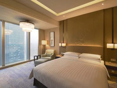 Luxurious modern hotel room with a king bed, floor-to-ceiling windows, and elegant lighting fixtures.