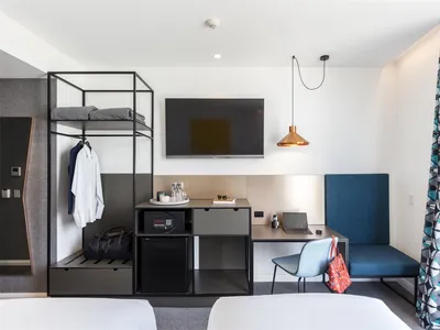 Modern minimalist hotel room with black metal frame cabinet, wooden desk, and fabric seating.