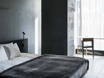 A minimalist bedroom with a concrete headboard, white bedding, and a dark grey blanket.
