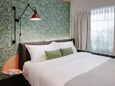 A minimalist hotel room with a bed featuring white cotton bedding, lace curtains, metal headboard, and glass window.