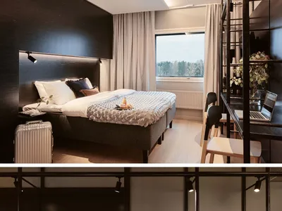 A modern hotel room featuring a black accent wall, a comfortable bed, and a sleek desk area with a wardrobe.