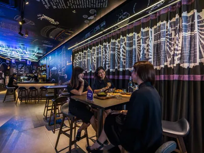 Three women sitting at a table in an industrial-style restaurant with metal, glass, and concrete elements.