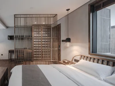A minimalist bedroom featuring a wooden bed and furniture, with large windows and a hanging lamp.