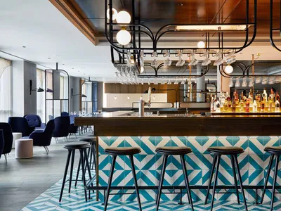 A modern bar interior with a blue and white tile floor and black stools.