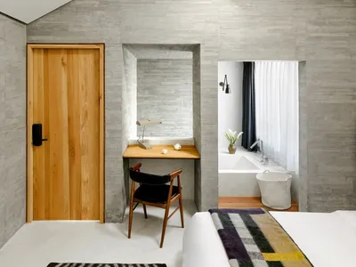 A modern minimalist bedroom featuring a concrete wall and a window with a white curtain.