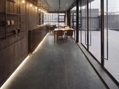 An industrial-themed restaurant interior with concrete walls, wooden furniture, and a long central walkway lined with tables