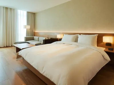 Modern minimalist bedroom featuring a white bed with wood furniture and a wooden floor.