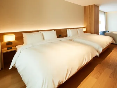 A modern hotel room featuring white beds with wooden headboards and wooden flooring.