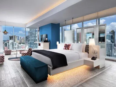 Modern hotel room interior with wooden furniture, fabric accents, glass walls, and metal elements.