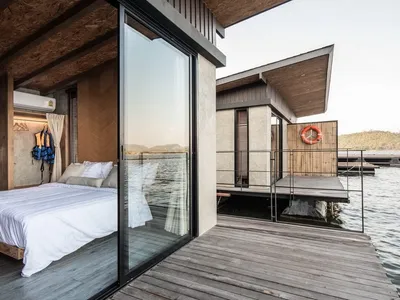 Modern floating hotel room with wood flooring, concrete walls, and large glass windows showing a serene water view.