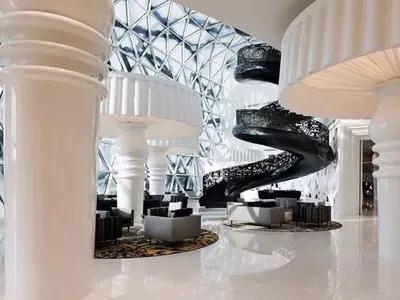 Modern hotel lobby featuring white marble flooring, black metal spiral staircase, and contemporary seating.