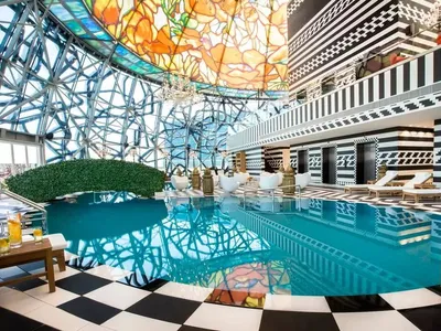 Modern hotel pool deck featuring glass and metal structural elements and a vibrant stained glass ceiling design.