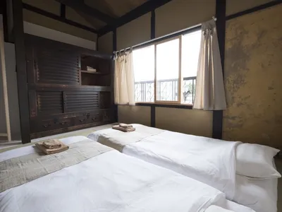 Minimalist bedroom with white bedding and wooden accents, featuring a large window with beige curtains, and a rustic wooden c