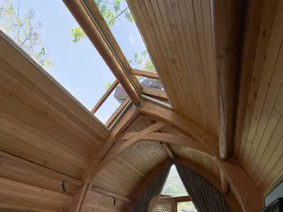 A stylish, wooden bedroom with arched ceiling, large windows, and a comfortable bed.