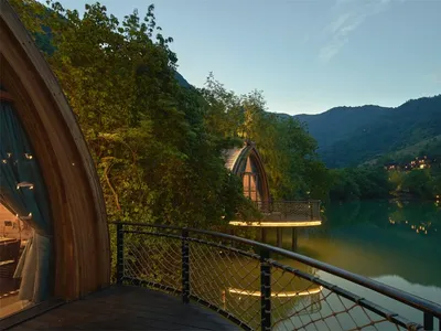 Hotel room with arched window overlooking tranquil water and mountains at dusk, built on stilts over calm lake.