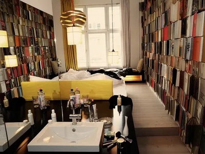 A minimalist bedroom filled with books on the walls and a bed with a bright yellow headboard.