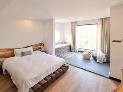 Minimalist bedroom featuring a bed with a wooden headboard and platform, a large window with a view, and a modern design.