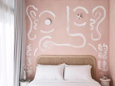 Pink wall with white paint strokes and symbols above the rattan headboard of a double bed.