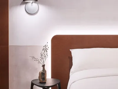 簡約臥室，棕色絎縫床頭板搭配白色床品，床上方擺放黑色小凳，凳上置一小花瓶