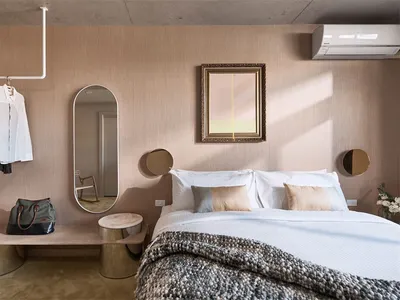 A modern bedroom featuring a bed with white bedding, a brown textured blanket, and mixed materials in the decor, including a
