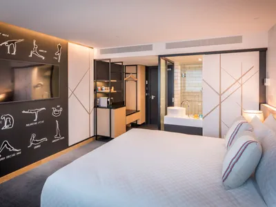 Modern minimalist hotel room with white bed, black accent wall, and open bathroom layout.
