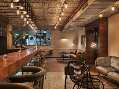 A modern bar interior featuring a wooden counter, contemporary lighting fixtures, and stylish seating arrangements.