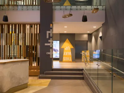 A modern hotel lobby featuring hanging lights, wood, concrete, and glass materials.
