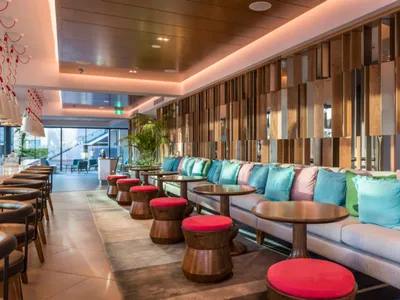 Contemporary lounge area of a hotel with wooden structures, fabric seating, and colorful throw pillows.