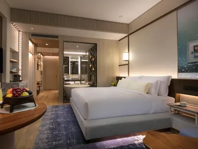 A modern hotel room featuring a large bed, a fruit basket, and a bathtub.