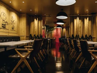 A dimly lit cafe interior with dark wooden tables and chairs, white walls, and red signage.